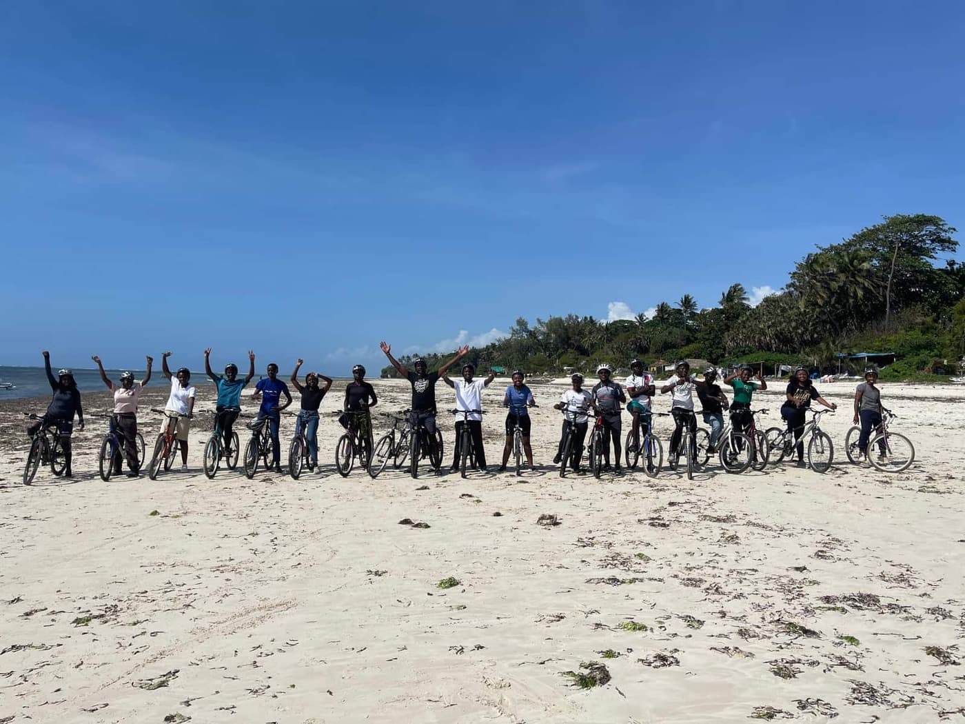 A line of riders with their bikes on the sand at Nyali beach, arms in the air