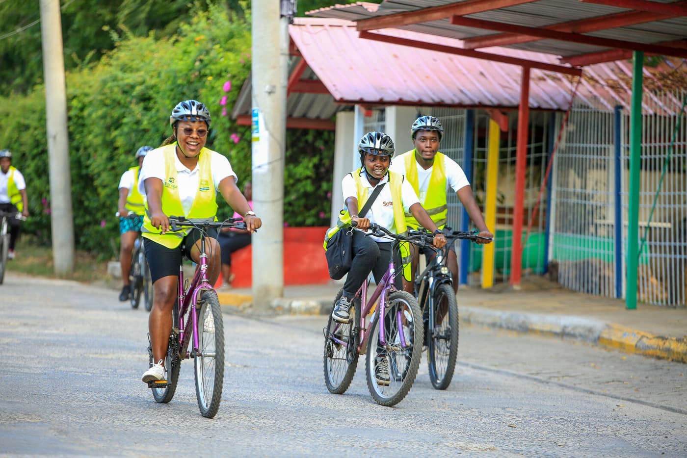 Riders in hi-vis vests cycling along a leafy Nyali road past a red-roofed building