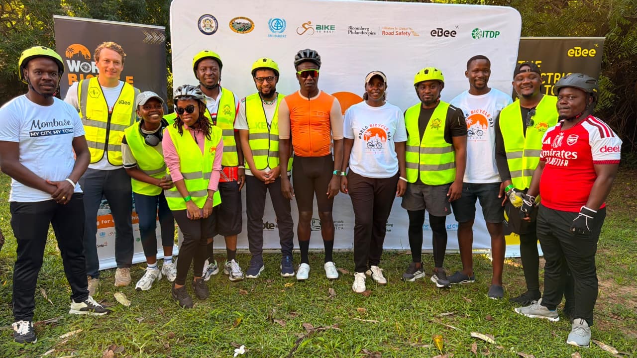The ride crew posing in front of the World Bicycle Day partners' backdrop on the grass
